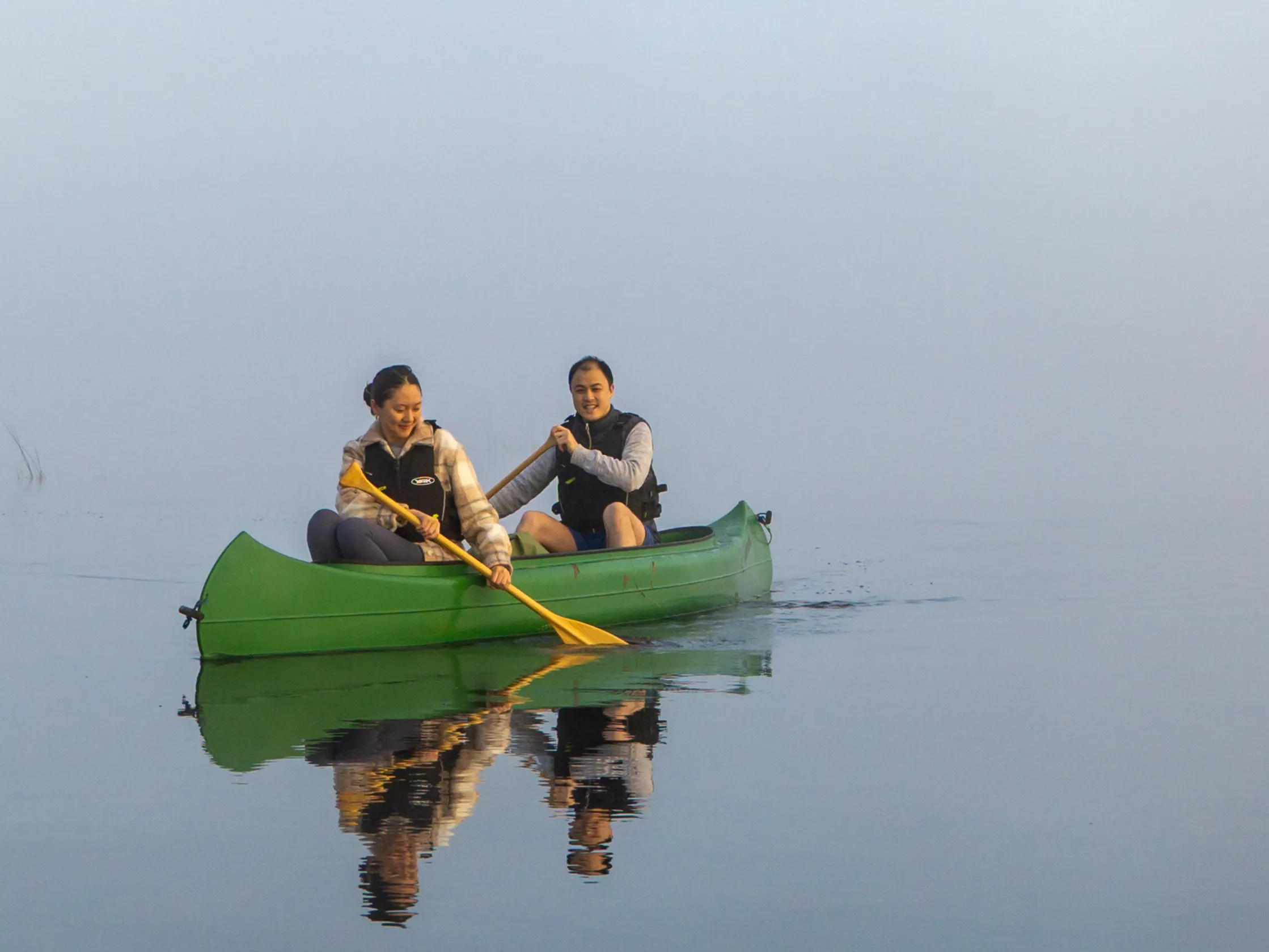 Two paddlers in a green canoe on calm, misty water